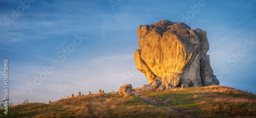 panoramic view to hill with huge rock in golden light under blue sky with copy space