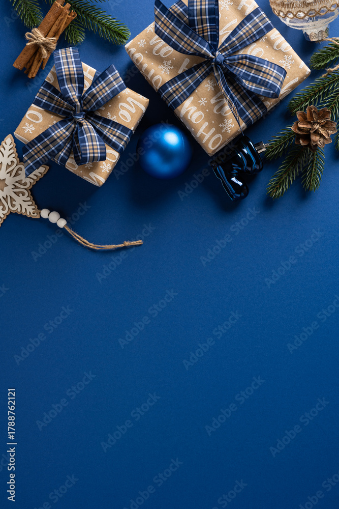 Naklejka premium Vibrant vertical Christmas scene featuring neatly wrapped gifts with blue plaid ribbons, pine cones, ornaments, and holiday decor on a deep blue background