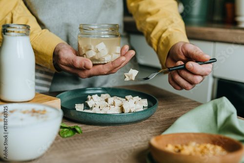 Males hands holding tofu on a fork over a jar