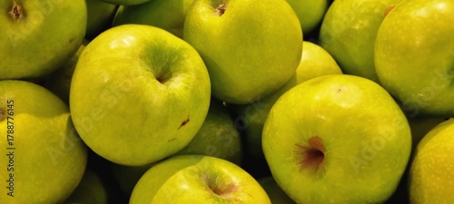 Vibrant close-up photograph of a pile of fresh green apples, showing their smooth texture and natural shine