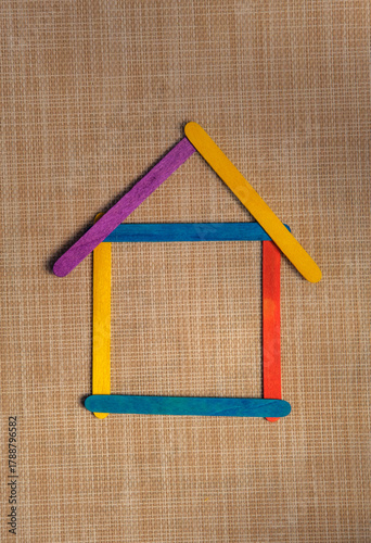 Creative house shape made from colorful wooden popsicle sticks on a textured fabric background. Symbolizing home, education, creativity and playful geometric art for children’s learning.