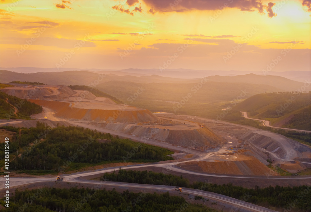 Fototapeta premium Aerial view of expansive open pit mine at sunset with stunning horizon and forested landscape