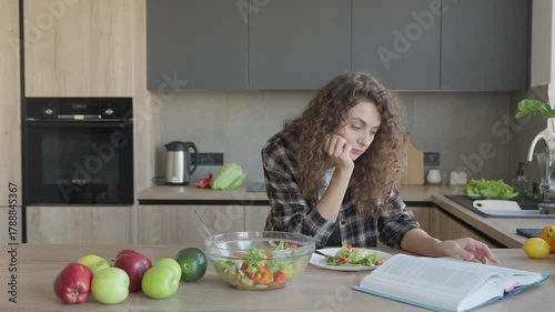 Woman Reading Book While Eating Fresh Salad In Modern Home Kitchen