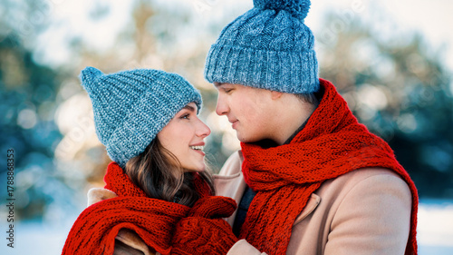 Fotografie A young couple stands close, smiling at each other in a snowy landscape