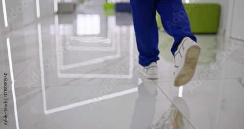 Close-up of doctor in blue pants and white shoes walking across a clean floor in the corridor of a modern hospital