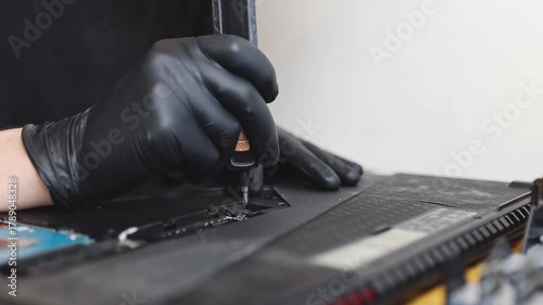 A man unscrews a bolt on a laptop with a screwdriver.