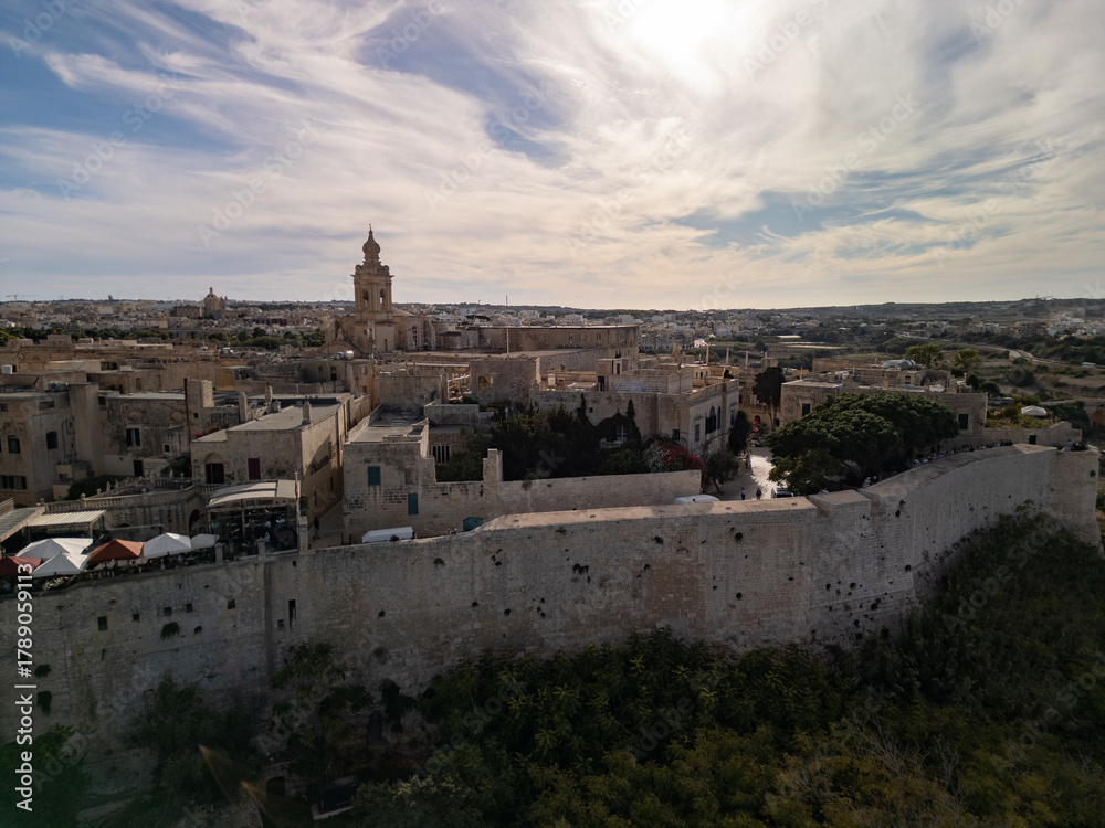 Fototapeta premium High altitude aerial view of Mdina old town at sunset, the Silent City with yellow limestone walls and St. Paul's Cathedral, scenic drone shot in Malta.