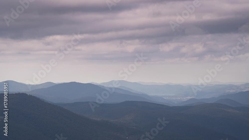 Time lapse of grey clouds moving across the sky with patterns of sunlight passing over blue mountains below,