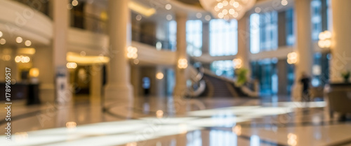Blurred modern hotel lobby interior with warm color tones, polished surfaces, and structured lighting. Depth of field highlights architectural lines, suitable for hospitality backgrounds.