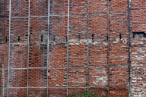 Aged Red Brick Wall with Visible Flaws and Metal Reinforcements in Vertical Lines
