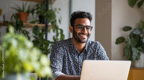 Smiling indian business man working on laptop at home office. Young indian student or remote teacher using computer remote studying, virtual training, watching online education webinar at home office
