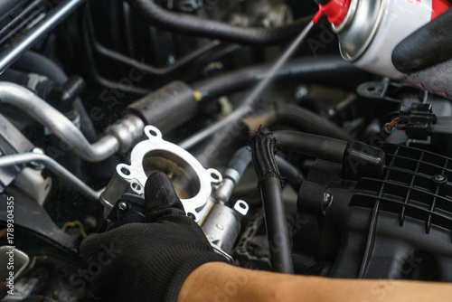 Auto mechanic cleaning a vehicle's throttle body. Technician uses a spray cleaner for engine maintenance in a repair shop.