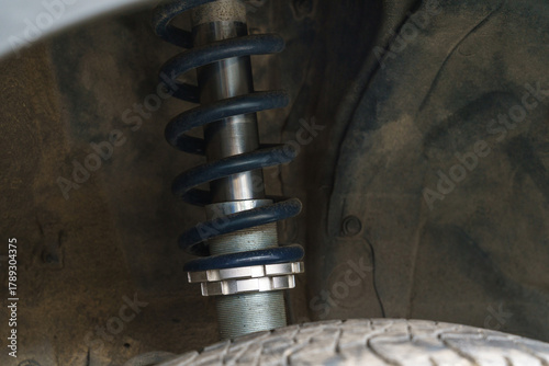 Detailed close-up of a dirty adjustable coilover suspension and spring mounted on a car. Automotive part and vehicle tuning concept.