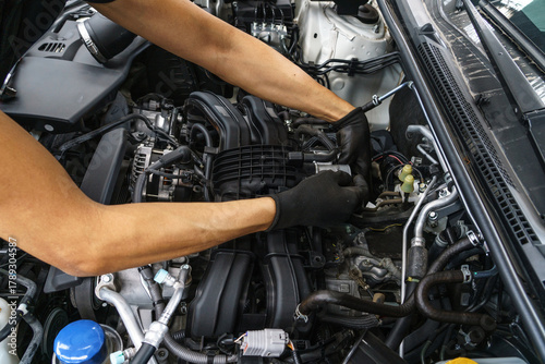 Unrecognizable auto mechanic wearing gloves uses a tool to service a modern car engine in a repair shop. Professional vehicle maintenance concept.