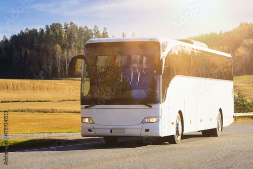 White coach bus at speed on road on a sunny autumn afternoon, blue sky and clouds.