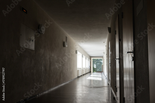 Obraz na płótnie A quiet, dim corridor with closed doors on the right and natural light at the fa