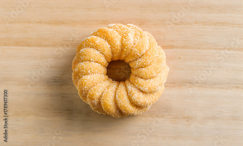 A single delicious sugar-coated cruller donut with a swirled ridged texture, presented as a morning breakfast treat on a light wooden table background in a top-down view