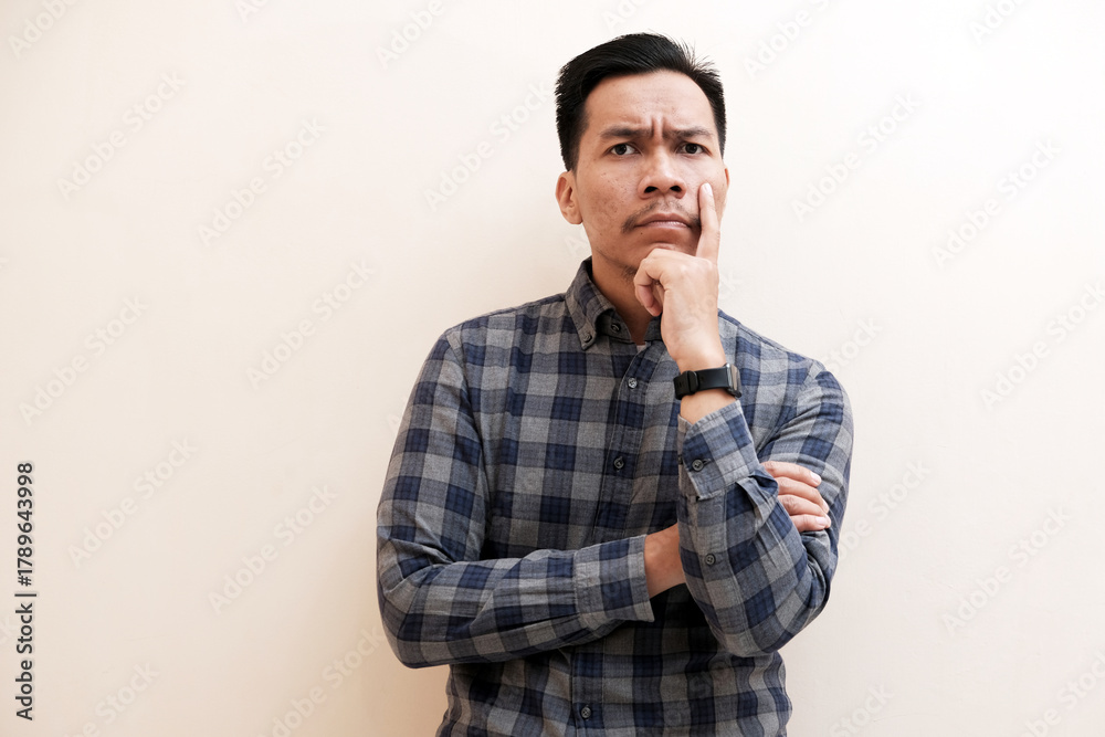 Obraz premium Southeast Asian man wearing flannel shirt thinking about something while looking to upper right corner, on white isolated background