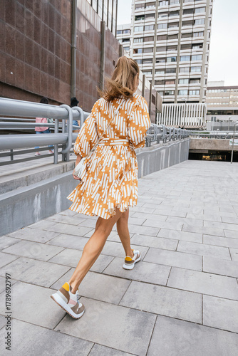 Woman walking away wearing orange dress and sneakers.