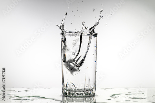 A glass of water with ice cubes in it is splashing water out of the glass