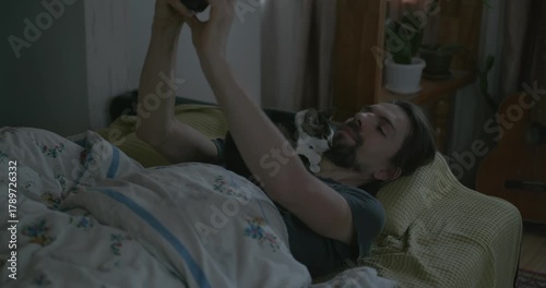 Man Waking up in Bed with Smartphone and Kitten. 4K 10-bit