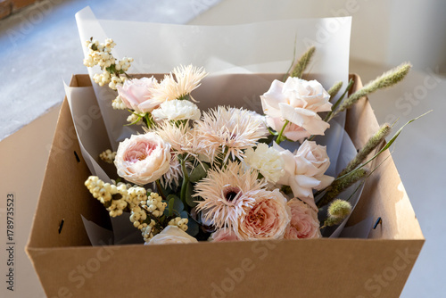 Fotografie Delicate pastel bouquet with blush pink garden roses, white fringed flowers, and dried accents, carefully packaged in a brown cardboard box for flower delivery