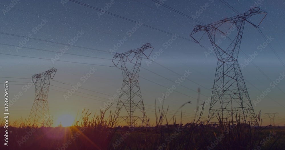 Obraz premium Silhouetting three high-voltage towers and power lines over rural field at sunset with tall grasses