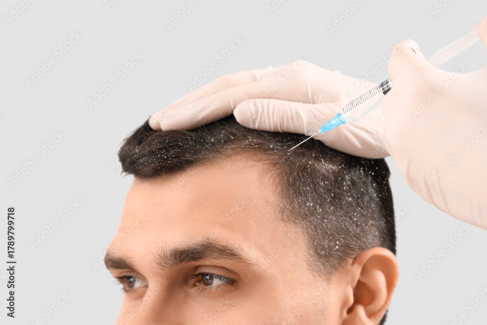 Naklejka premium Young man with dandruff receiving injection from trichologist on light background, closeup