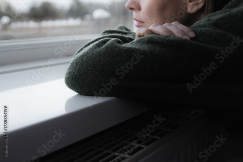 Thoughtful sad woman sitting on a windowsill. Mental health and seasonal disorder. Winter scenery outside