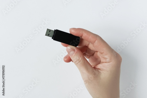 A black USB flash drive held by a Caucasian woman. White background.