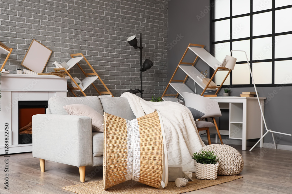 Fototapeta premium Interior of messy living room with grey sofa and overturned furniture after earthquake