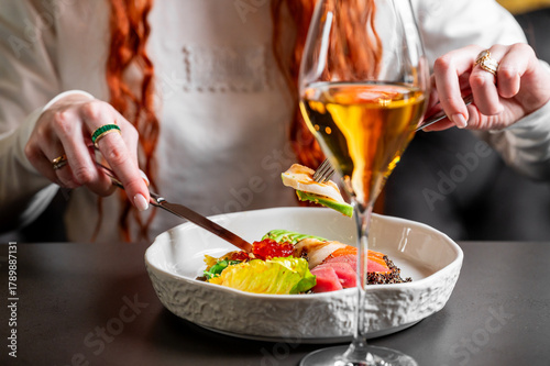 Close-up of a person enjoying a luxurious seafood appetizer (tuna, avocado, caviar) paired with sparkling amber wine in a chic restaurant setting. Fine dining experience