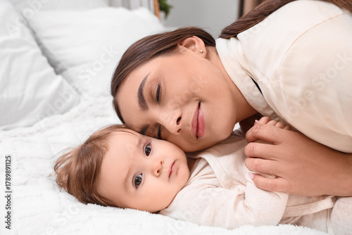 Young mother in pajamas hugging her baby on bed at home, closeup. Internation...