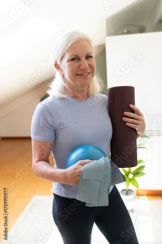 Active woman holding pilates mat and ball indoors during fitness exercise