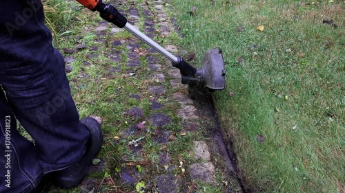 Close-up of man trims grass along curb with cordless hand-held lawn trimmer with line. High quality 4k footage