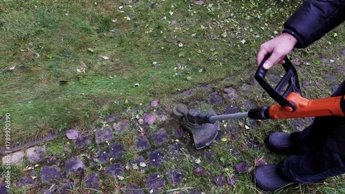 Close-up of man trims grass along curb with cordless hand-held lawn trimmer with line. High quality 4k footage