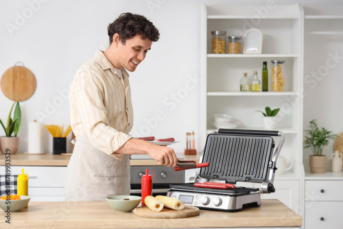 Young man grilling sausages for hot dogs in kitchen