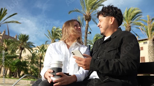 Young couple using a smartphone and laughing on a park bench