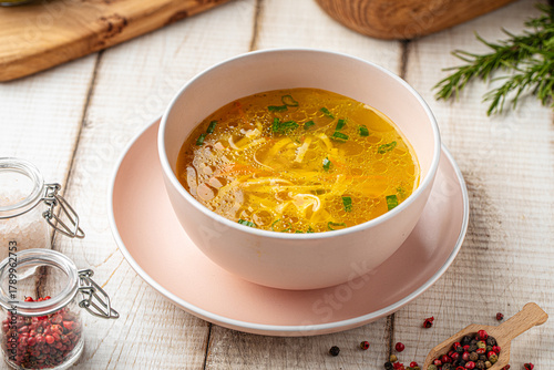 Hot chicken noodle soup with fresh herbs served in a pink bowl on a wooden table