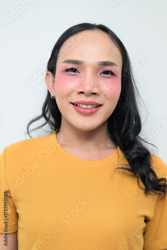 Portrait of a young happy Thai transgender person against white background smiling