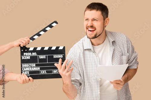 Male actor and female hands with movie clapper on beige background