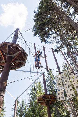 Adventure park challenge in forest setting with safety gear and suspended rope