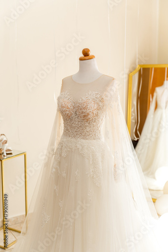 A beautiful bridal gown showcases intricate lace details and sheer fabric in a well-lit fitting room. The gown is displayed elegantly, capturing the essence of bridal elegance.