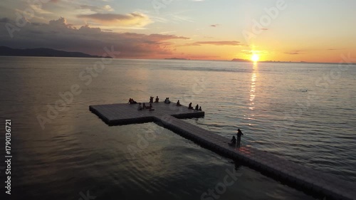 sunset over swimming pier with people low drone shot over koh phangan coastline captures