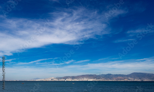 Fototapeta Naklejka Na Ścianę i Meble -  Storm clouds gather over a distant coastal landscape. Cloud patterns form against a calm sea and a deep blue sky.