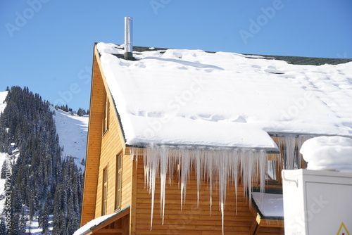 A wooden house covered with a large layer of ice and icicles. Mountainous terrain. The guest house.