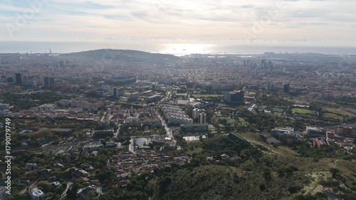 Barcelona cityscape showcasing the diverse urban landscape from an elevated perspective, featuring residential neighborhoods, sports facilities, and the sea under a clear sky