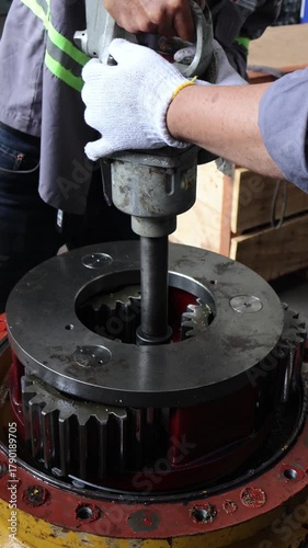 Industrial mechanics operating a heavy-duty pneumatic wrench or air impact on a large gear assembly of a final drive component during disassembly or critical maintenance in a repair workshop.