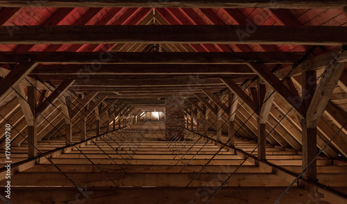 The interior of the attic of an old renovated building. Wooden structural elements and light from a window in the distance are visible. Background.