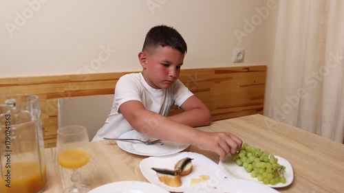 A boy eats and drinks juice while sitting at a table.
